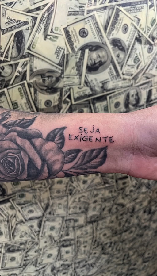 'SEJA EXIGENTE' em letras de forma no antebraço, ao lado da rosa tatuada
